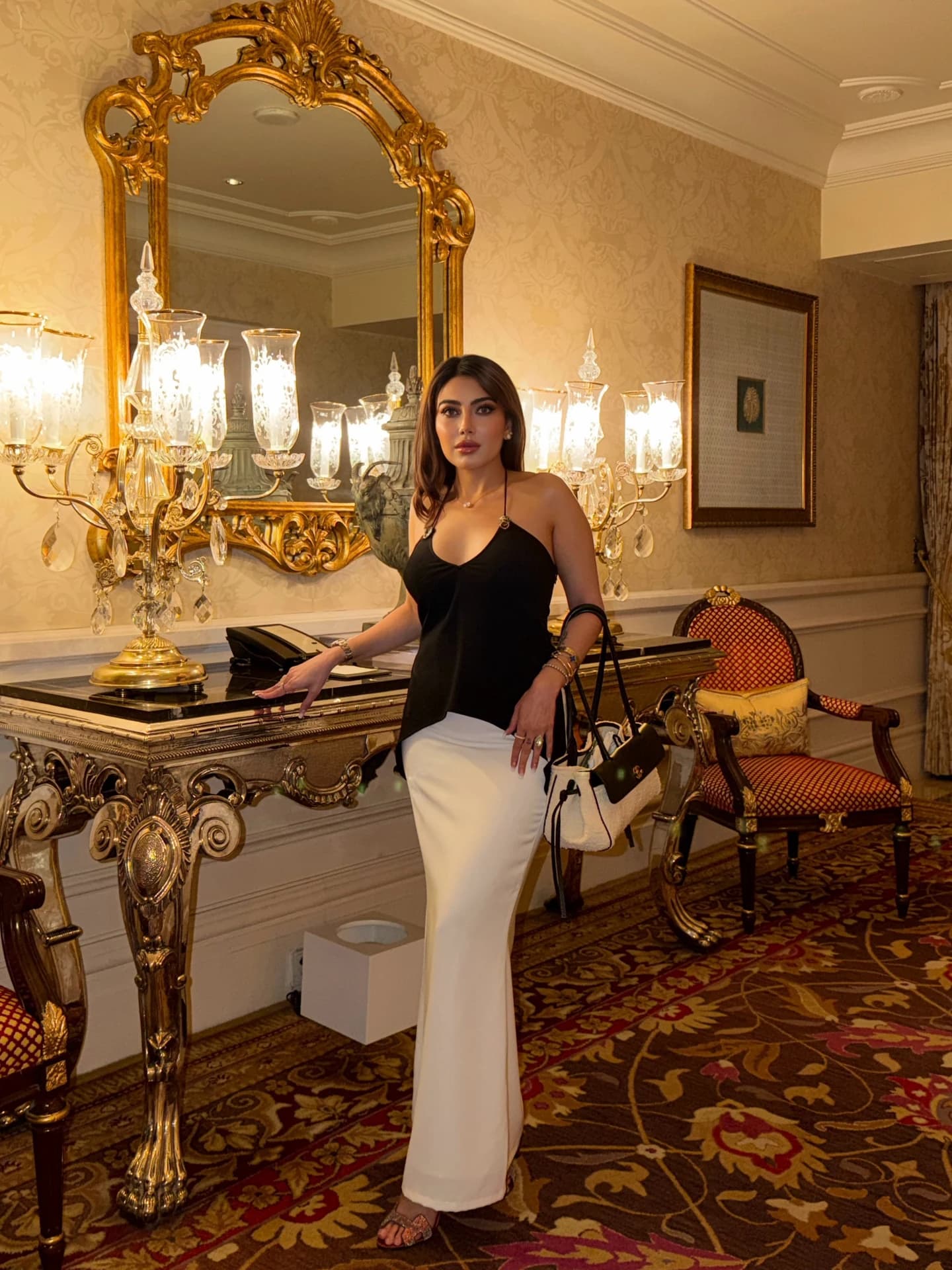 Karisma in a black and white outfit in a warmly lit interior